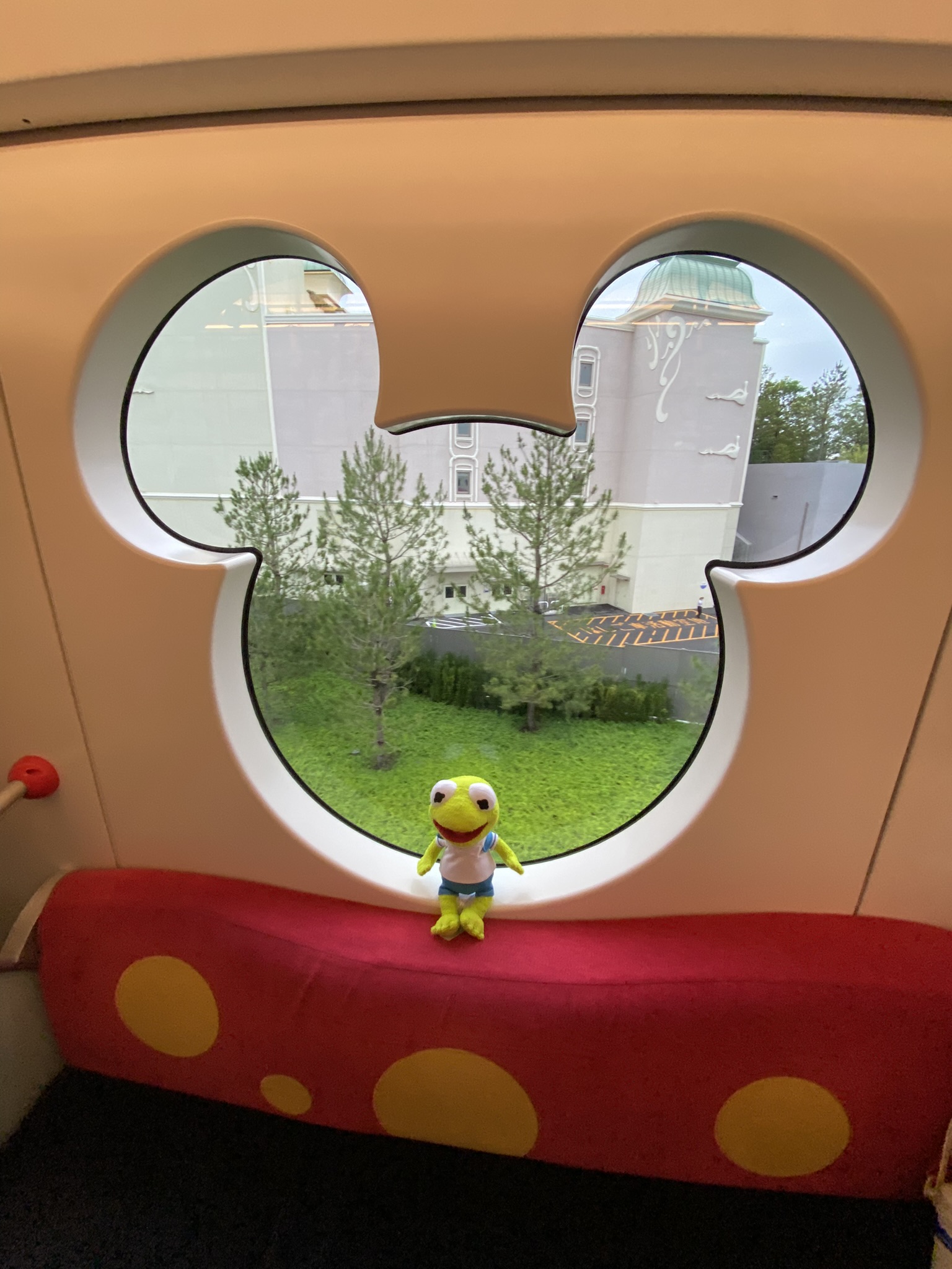 Kermit sitting in the windowsill of a Mickey-shaped window on a Disney train.