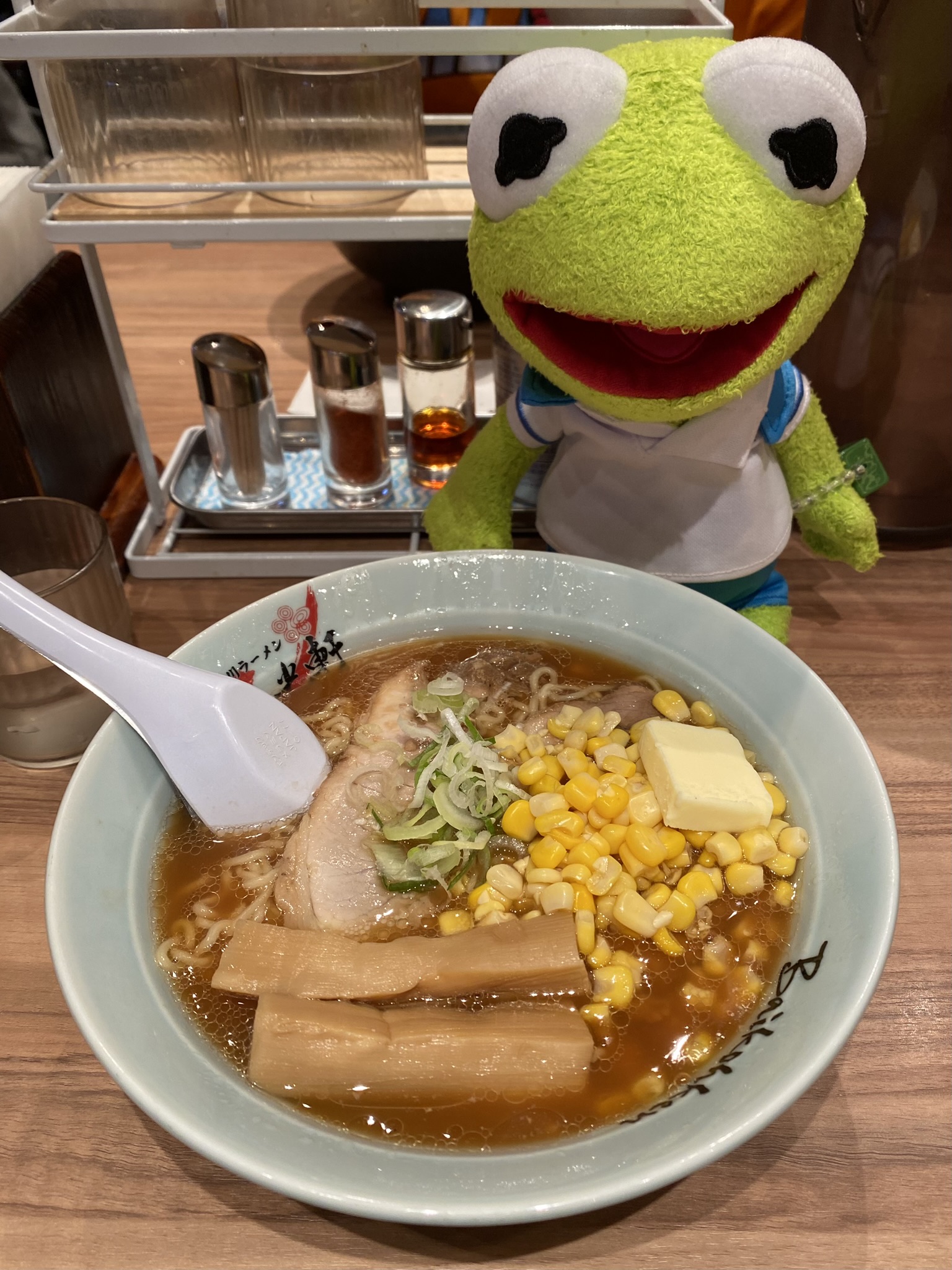 Kermit sitting next to a steamy bowl of butter corn ramen.