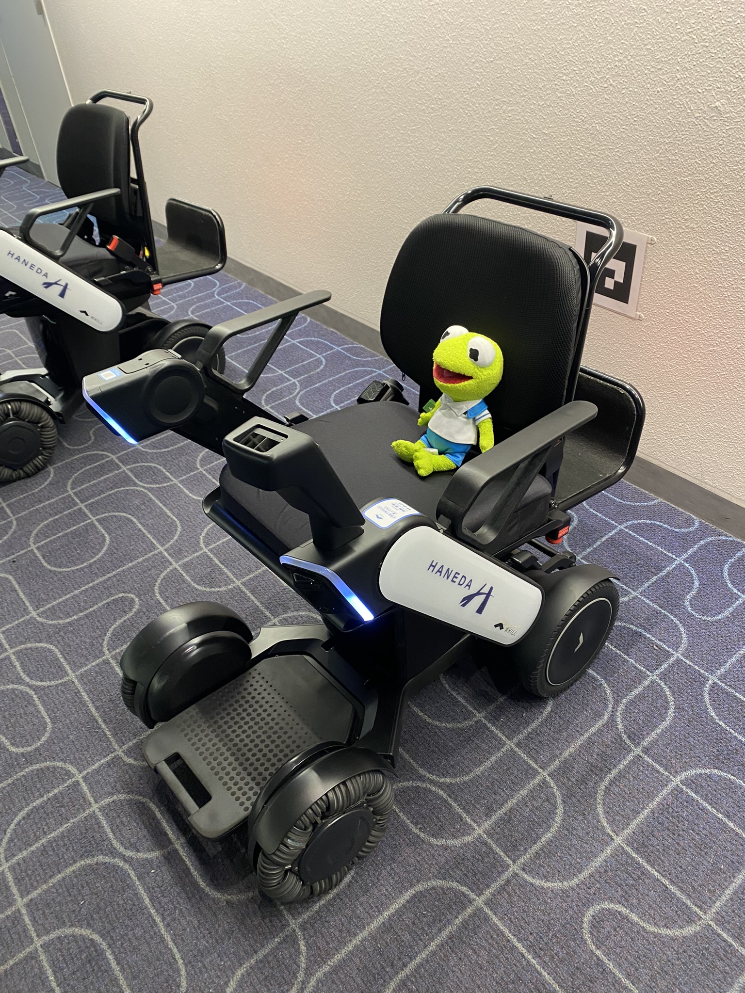 Kermit sitting in an electric, airpoirt wheelchair at Haneda Airport.