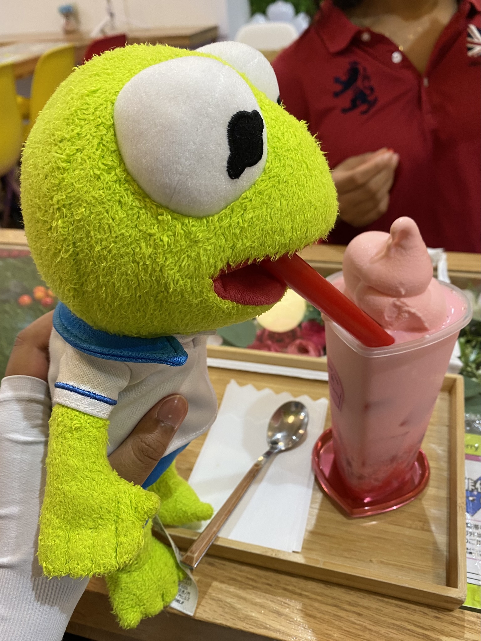 Kermit taking a sip of a bright pink, strawberry float with the straw in his mouth.