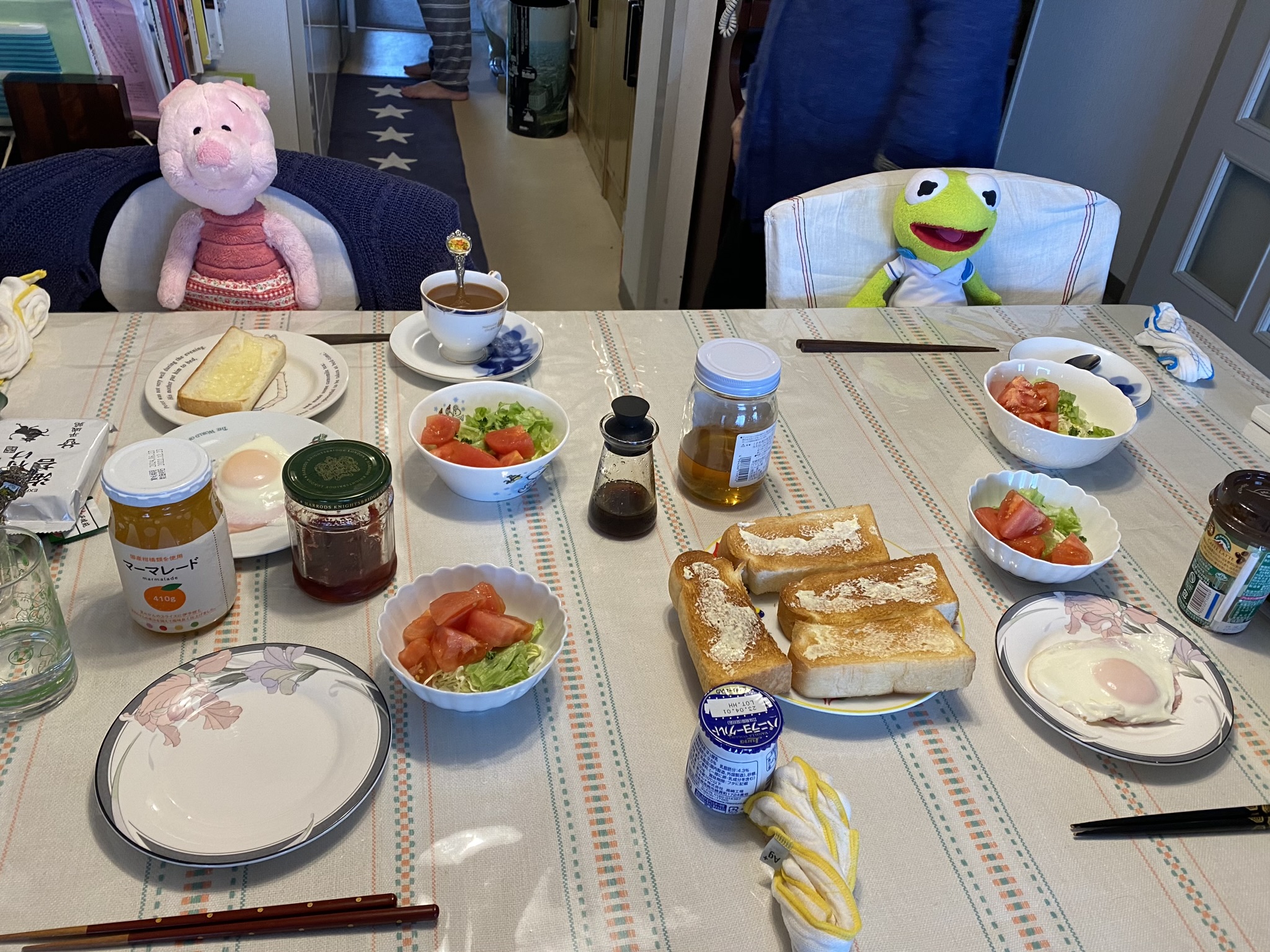 Kermit and Piglet sitting at the breakfast table in front of numerous plates of buttered toast, salads, and eggs.