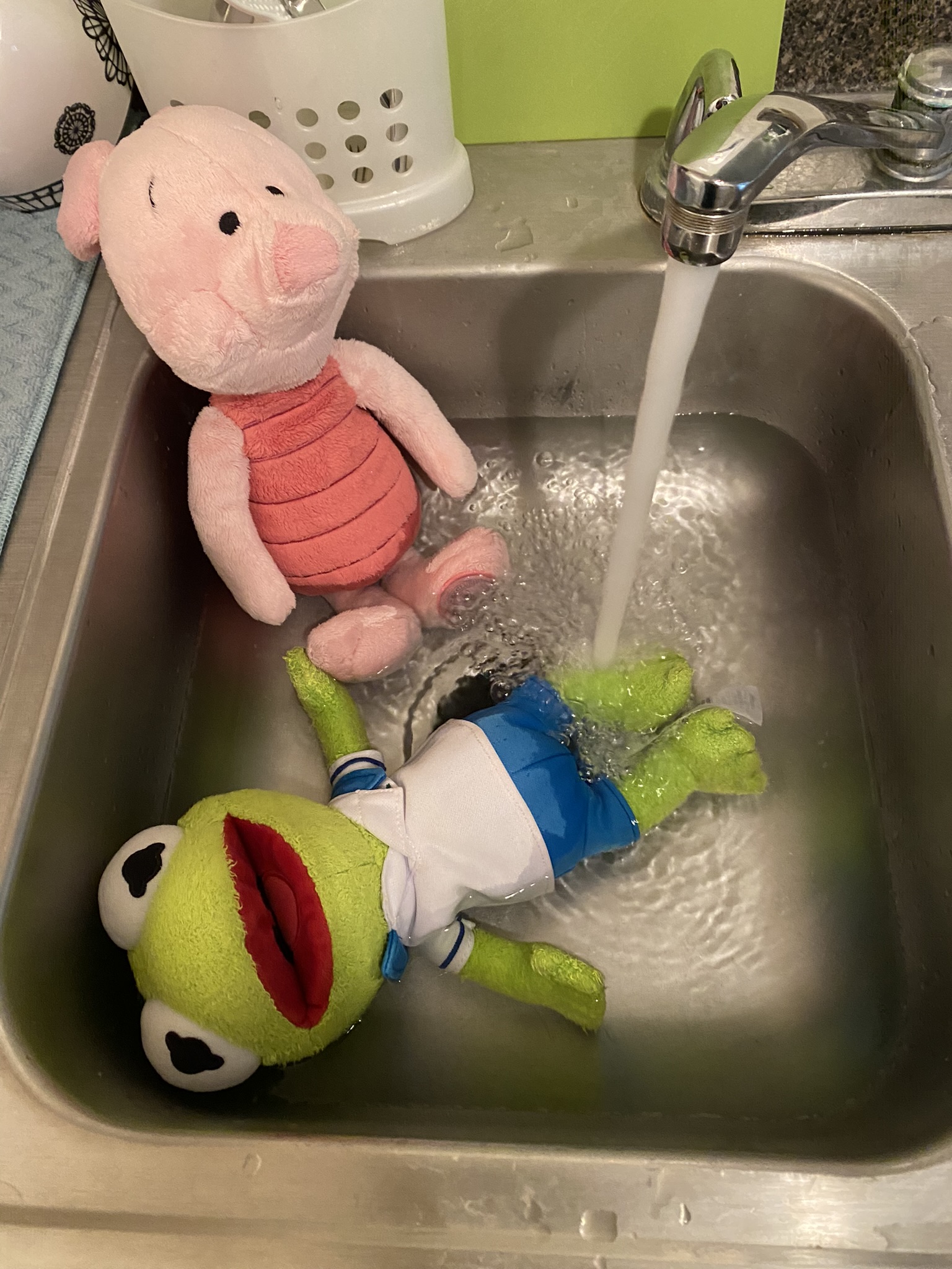 Kermit and Piglet sitting in a pool of water in the kitchen sink.