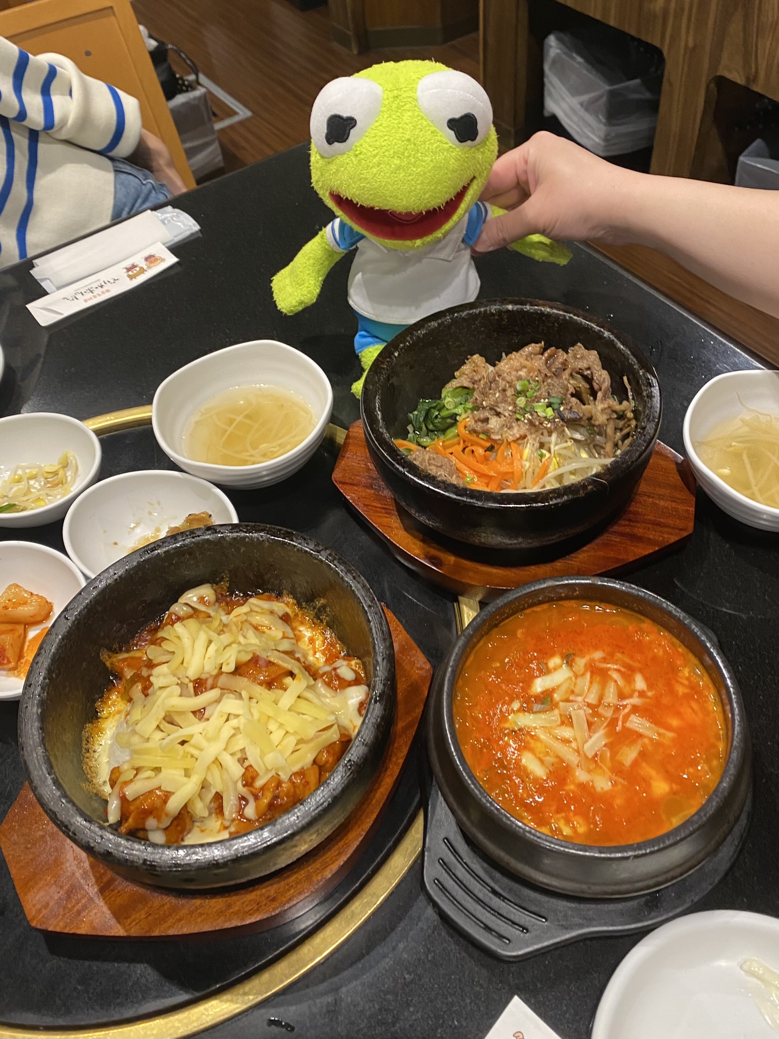 Kermit sitting by many bowls of savory Korean food.