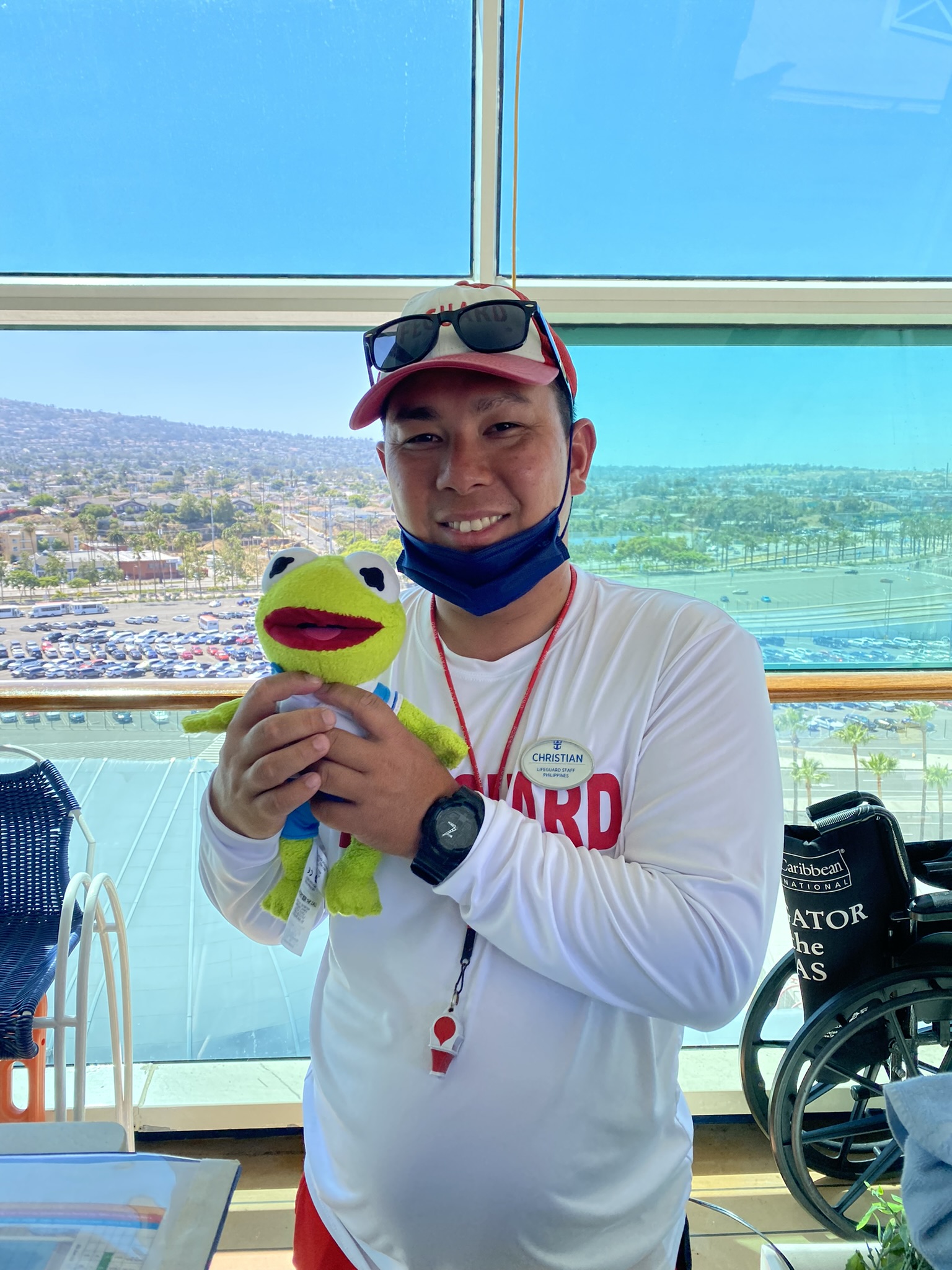 Kermit being held by a man wearing a lifeguard shirt and a whistle around his neck.