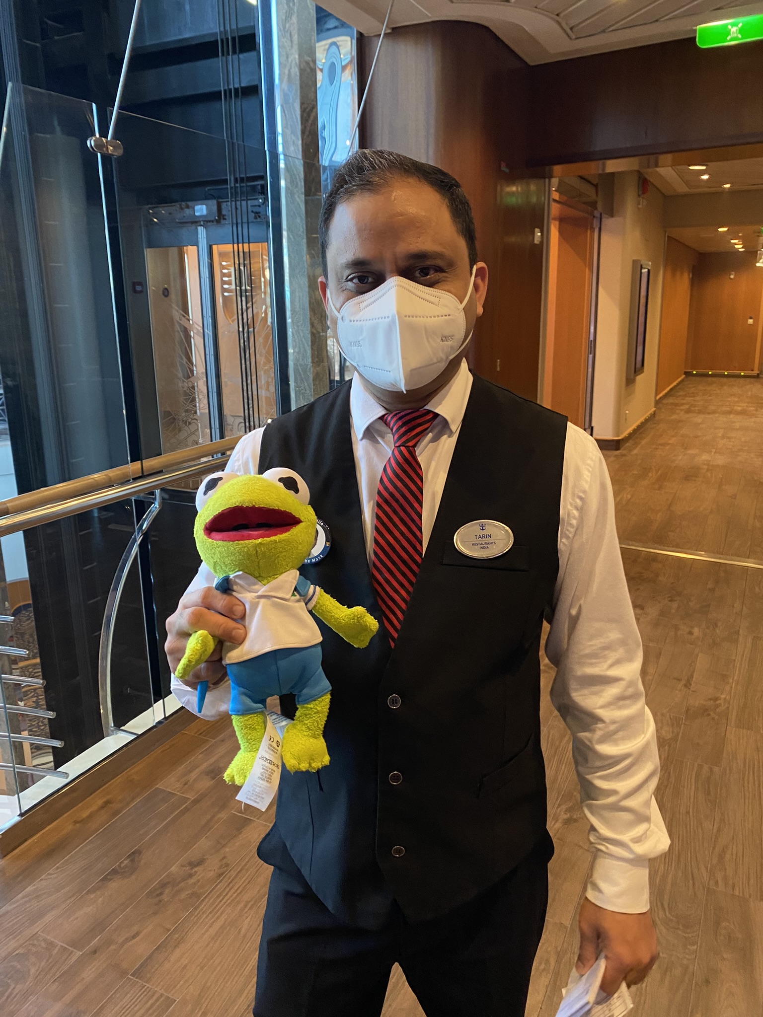 Kermit being held by a man wearing a vest and tie.